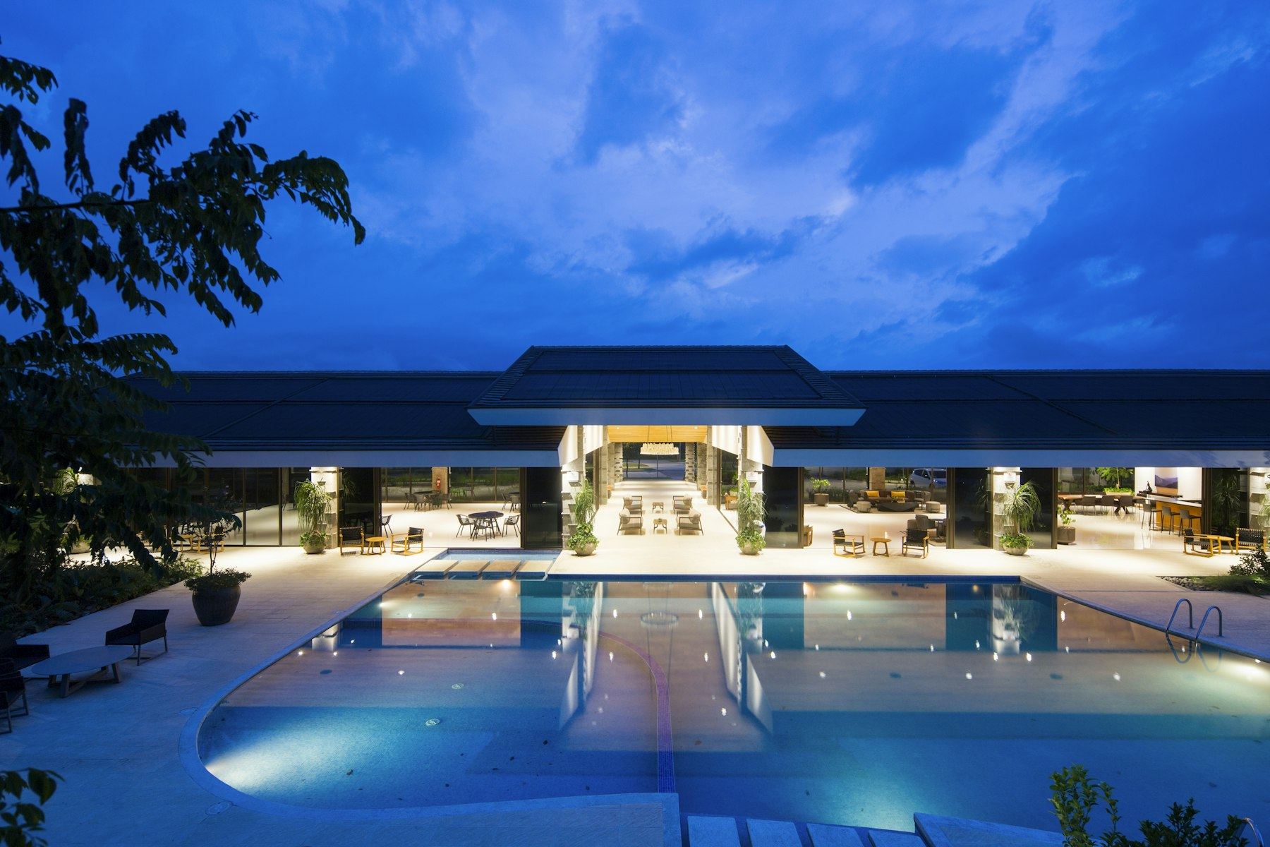 A contemporary hotel exterior lit at dusk, with a pool in the foreground
